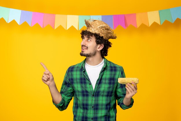 Festa junina giovane ragazzo carino con cappello di paglia e bandiere colorate festival brasiliano guardando in alto con mais