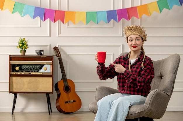 Festa junina ragazza carina con cappello di paglia brasiliano di mezza estate con chitarra radiofonica retrò che punta alla tazza rossa