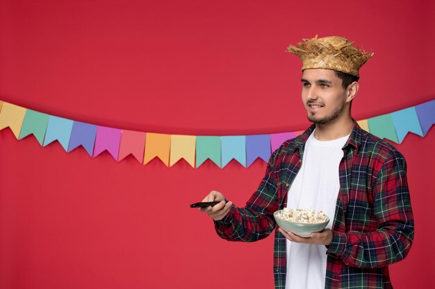 Festa junina sorridente ragazzo carino che indossa un cappello di paglia che celebra il festival brasiliano guardando la tv