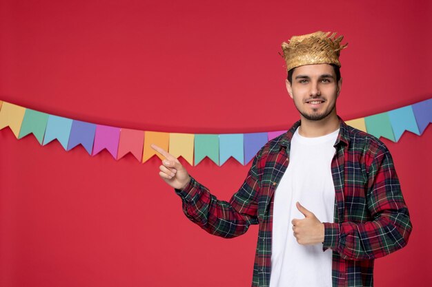Festa junina sorridente ragazzo carino che indossa un cappello di paglia che celebra il festival brasiliano indicando qualcuno