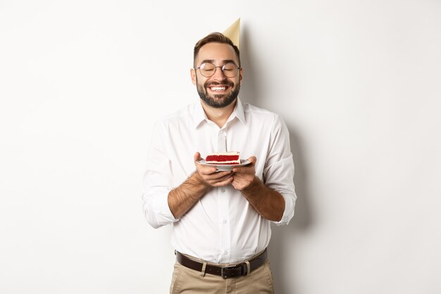 Feste e celebrazioni. Uomo felice che ha festa di compleanno, esprimere il desiderio sulla torta b-day e sorridente, in piedi