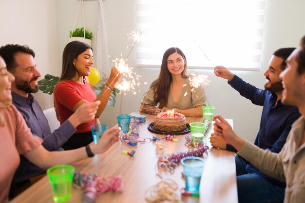 Festeggiamo insieme il tuo compleanno. Gruppo eterogeneo di amici che accendono le stelle filanti durante una festa di una giovane donna sorridente e si divertono molto