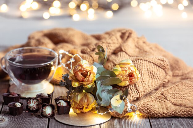 Festosa vita ancora con un drink in una tazza, cioccolatini e fiori su un tavolo sfocato con bokeh.