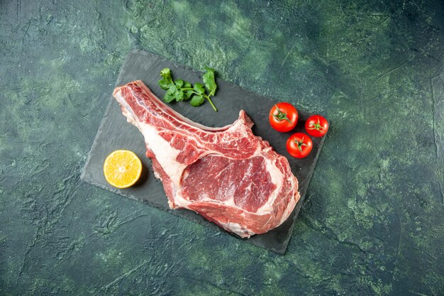 Fetta di carne fresca vista dall'alto con pomodori rossi su sfondo blu scuro cucina animale mucca cibo macellaio carne colore