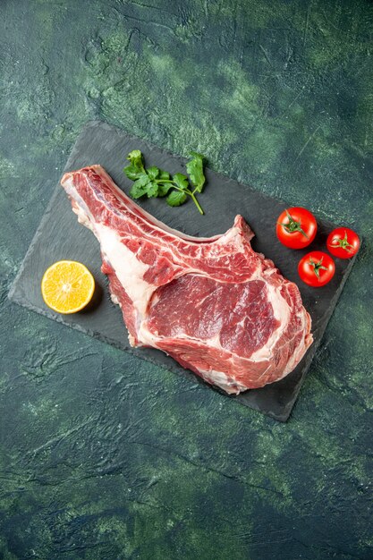 Fetta di carne fresca vista dall'alto con pomodori rossi su sfondo blu scuro cucina animale mucca cibo macellaio carne pollo colori