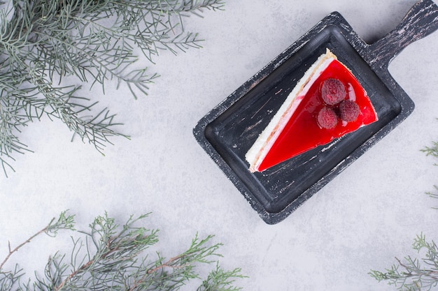 Fetta di cheesecake a bordo nero con ramo di pino.