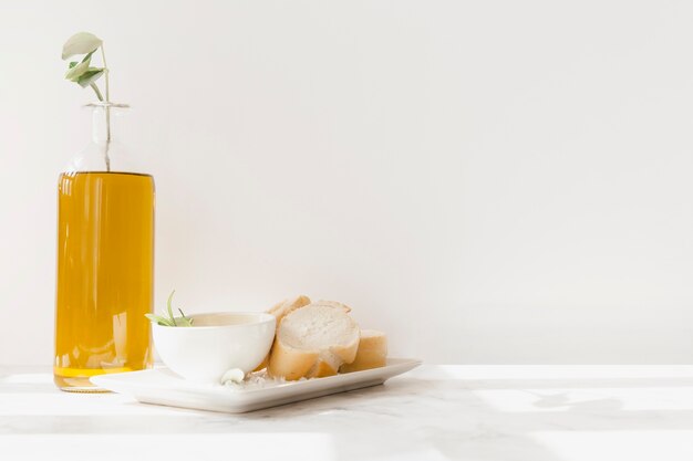 Fetta di pane con bottiglia di olio contro il muro bianco