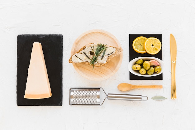 Fetta di pane con fetta di formaggio, rosmarino, olive e limoni su sfondo bianco