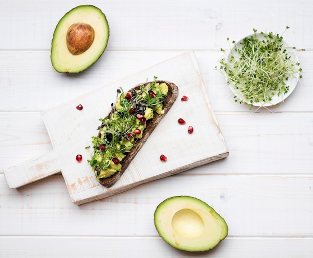 Fetta di pane con pasta di avocado e melograno su tavola di legno