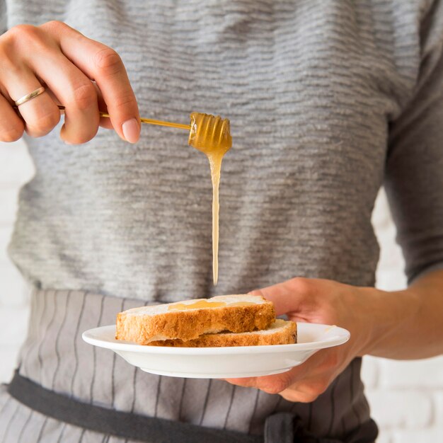 Fetta di pane di versamento del pane ober del miele della donna di vista frontale