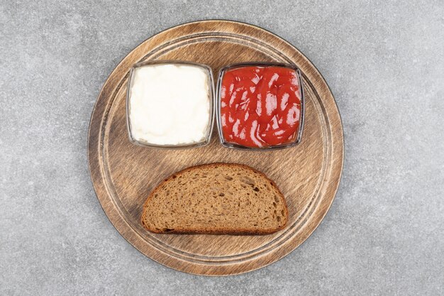 Fetta di pane nero, ketchup e maionese su tavola di legno