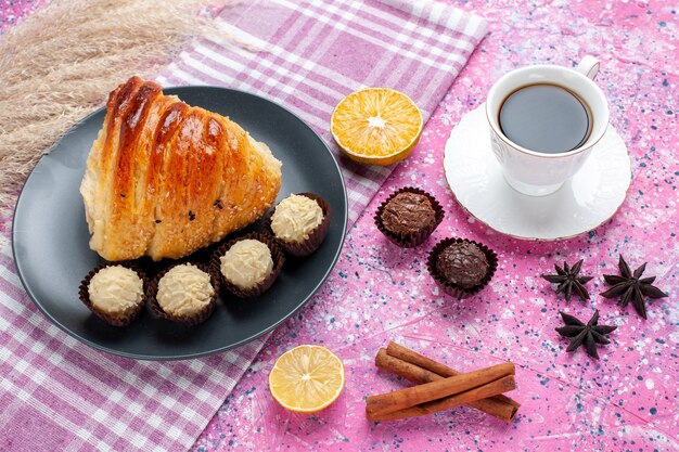 Fetta di pasticceria vista semi-superiore con cannella e cioccolatini su sfondo rosa.