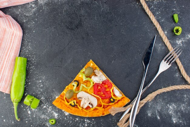 Fetta di pizza ai funghi vista dall'alto con pomodori rossi, olive verdi, funghi su tutto il tavolo grigio, pasta per pizza, carne italiana