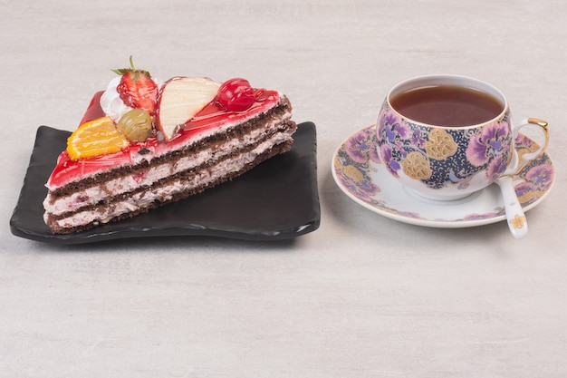 Fetta di torta al cioccolato sulla piastra con fette di frutta e tazza di tè.