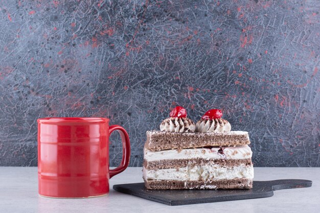 Fetta di torta sul bordo scuro con una tazza di tè sul tavolo di marmo. Foto di alta qualità