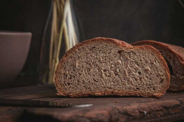 Fetta di vista laterale di pane sul tagliere e sul marrone scuro.