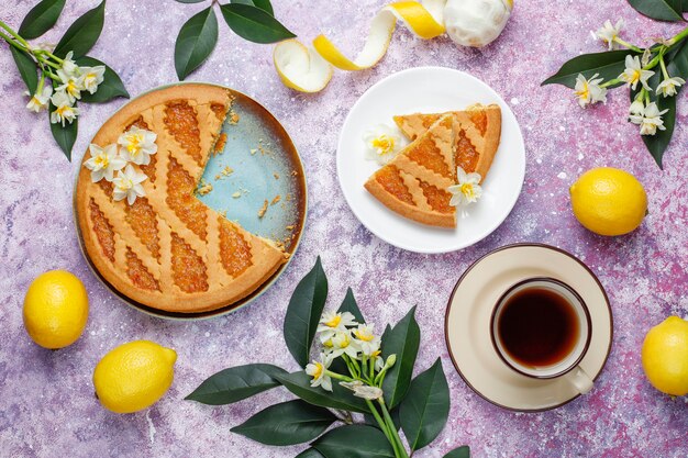 Fette deliziose della torta del limone con i limoni freschi e una tazza di tè, vista superiore