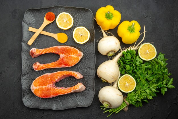 Fette di carne fresca vista dall'alto con verdure e limone su sfondo scuro