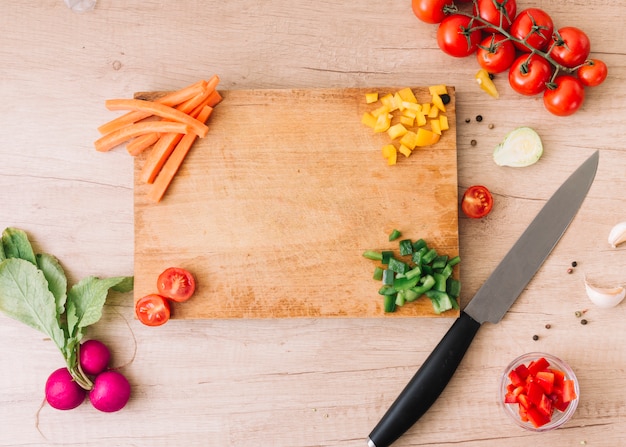 Fette di carota; peperone; pomodori; barbabietola; pepe nero e spicchi d&#39;aglio sulla scrivania in legno