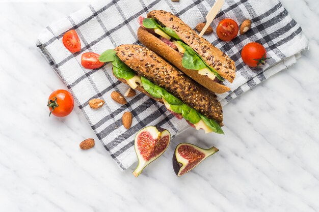 Fette di fichi; pomodori ciliegini; mandorle con hot dog freschi sopra un panno da cucina su sfondo bianco con texture