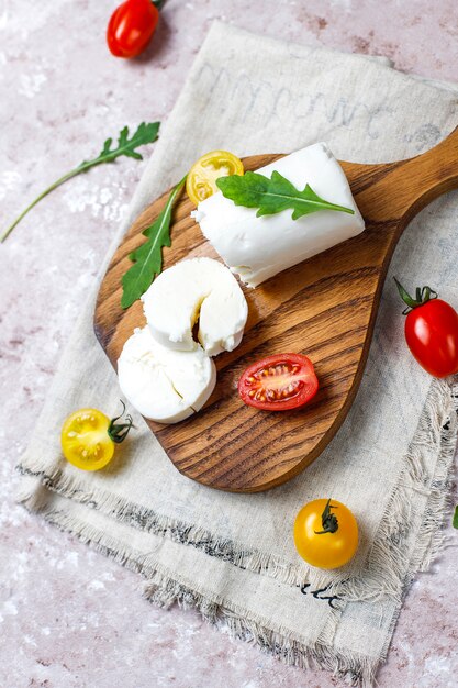 Fette di formaggio di capra su tavola di legno con rucola, pomodorini. Pronto a mangiare.