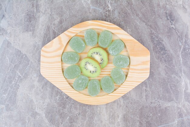 Fette di kiwi e caramelle di marmellata sul piatto di legno.