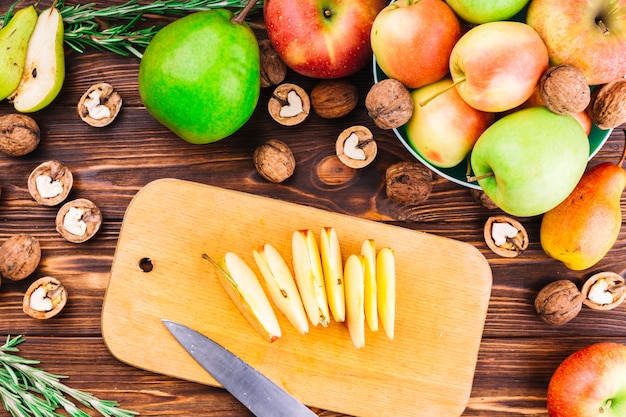 Fette di mela sul tagliere con frutta e noci sopra il tavolo