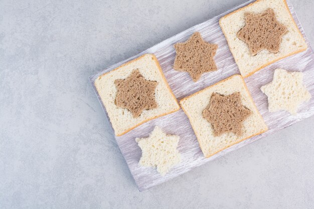 Fette di pane bianco e nero a forma di stella e quadrata sul piatto di legno