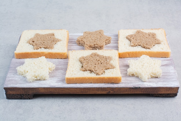 Fette di pane bianco e nero a forma di stella e quadrata sul piatto di legno