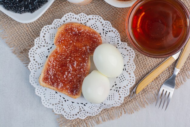 Fette di pane bianco fresco con marmellata e uova sode su fondo di marmo.