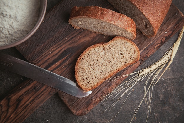 Fette di pane di vista laterale con il coltello sul tagliere e sul marrone scuro.