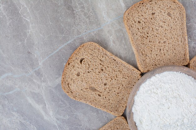 Fette di pane integrale con farina sulla superficie di marmo