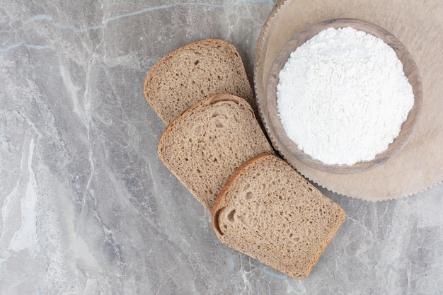 Fette di pane integrale con farina sulla superficie di marmo