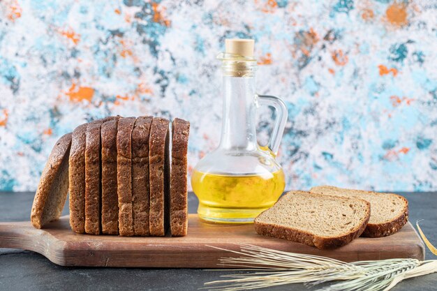 Fette di pane integrale e bottiglia di olio su tavola di legno.