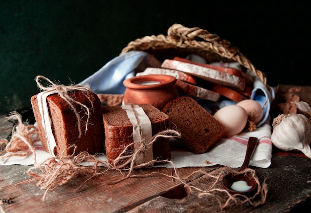 Fette di pane nero avvolte con carta bianca e filo rustico con una pentola di latte, uova e aglio su un asciugamano bianco.