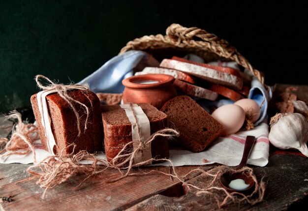 Fette di pane nero avvolte con carta bianca e filo rustico con una pentola di latte, uova e aglio su un asciugamano bianco.