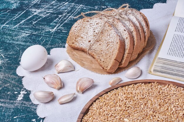 Fette di pane scuro con uova e aglio sul tavolo blu.