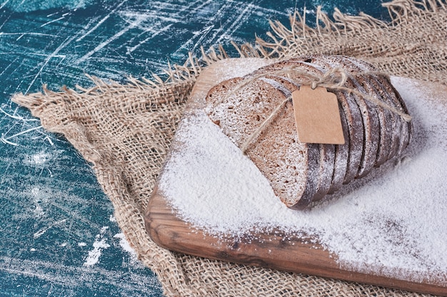 Fette di pane scuro sulla tavola di legno sul tavolo blu.