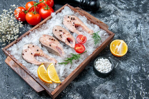 Fette di pesce crudo vista dal basso con ghiaccio su tavola di legno pomodori macinapepe sale marino sul tavolo