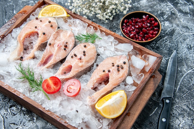 Fette di pesce crudo vista dal basso con ghiaccio su tavola di legno semi di melograno in un piccolo coltello a ciotola sul tavolo