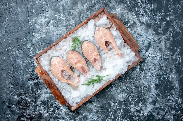 Fette di pesce crudo vista dall'alto con ghiaccio su tavola di legno su sfondo grigio posto copia