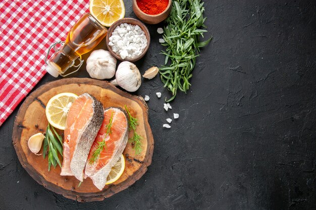 Fette di pesce fresco vista dall'alto con fette di limone aglio e condimenti sul tavolo scuro