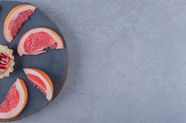 Fette di pompelmo fresco con cookie sul piatto di legno grigio