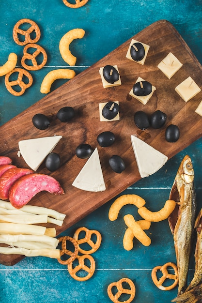 Fette di salsiccia con cubetti di formaggio, olive e cracker su una tavola di legno, vista dall'alto