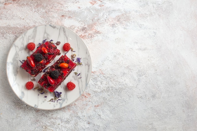 Fette di torta di frutti di bosco vista dall'alto con glassa cremosa rossa e frutti di bosco freschi su superficie bianca