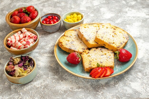 Fette di torta gustosa vista frontale con caramelle e frutta sulla torta dolce torta superficie leggera