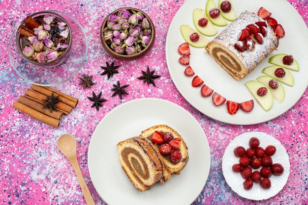 Fette di torta rotolo vista dall'alto con diversi frutti all'interno del piatto bianco con cannella anche sullo sfondo colorato torta biscotto colore dolce