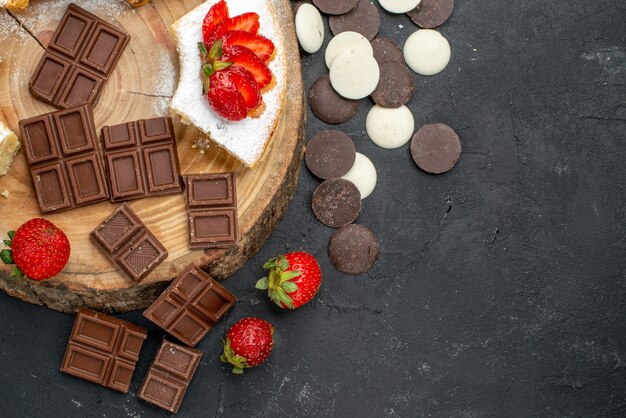 Fette di torta vista dall'alto con biscotti e barrette di cioccolato su uno sfondo scuro