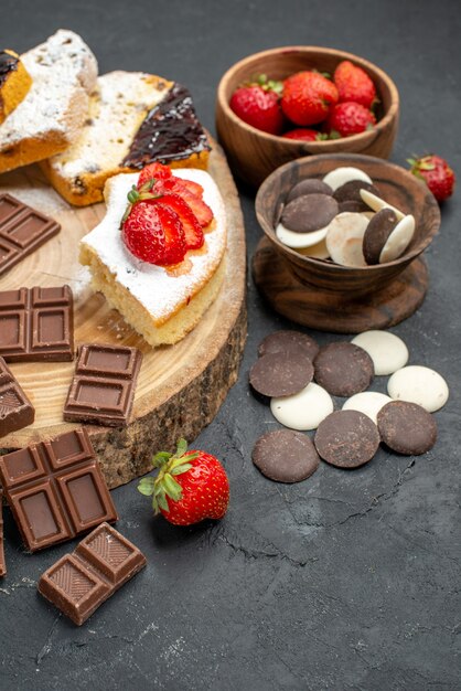 Fette di torta vista frontale con barrette di cioccolato e biscotti su sfondo grigio