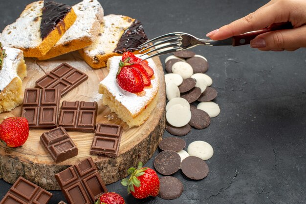 Fette di torta vista frontale con barrette di cioccolato e biscotti su sfondo scuro